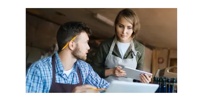Two employees in a medium business using HR software on laptop and tablet for workforce management and time tracking.