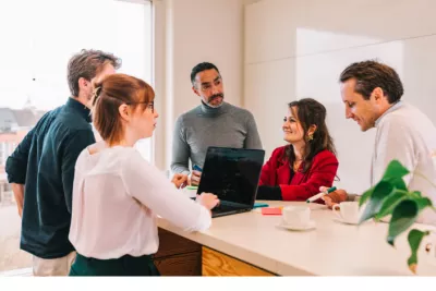 Group of colleagues in a meeting around a laptop in a bright office