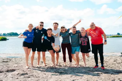 Eight colleagues in sportswear smiling and posing together on a sunny beach