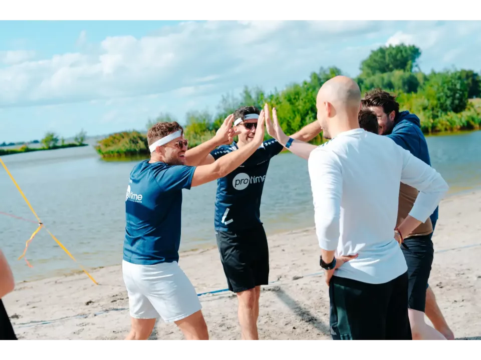 Group of colleagues on a beach celebrating with high-fives near the water.