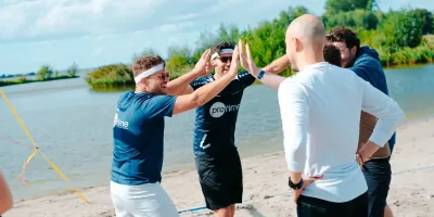 Group of colleagues on a beach celebrating with high-fives near the water.